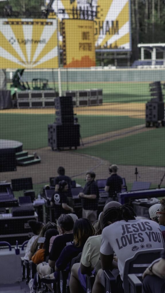 Lit stage on a baseball field at dusk with crowd